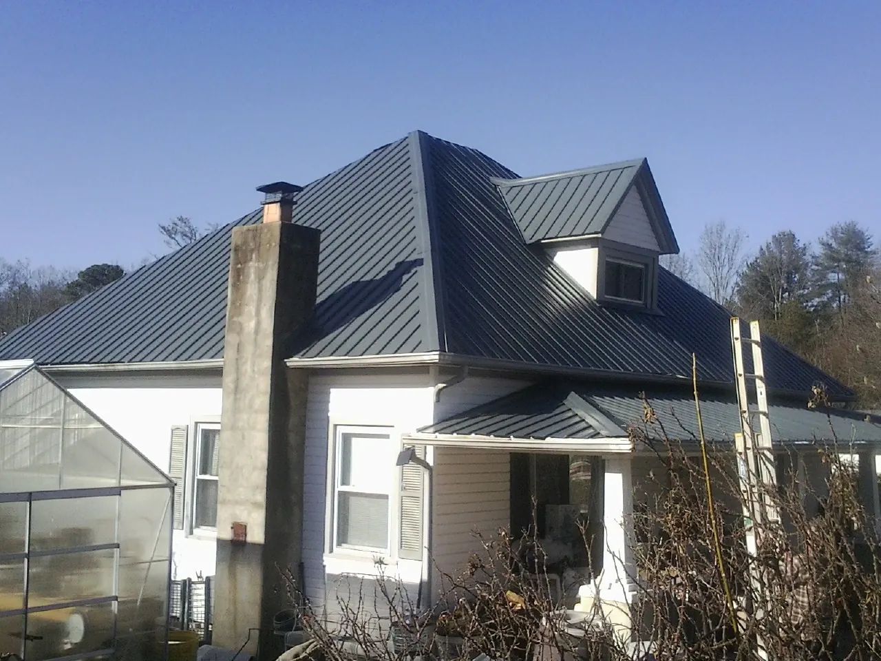 Dark blue standing seam metal roof on a white farmhouse with dormer — Slate & Tile Roof Repair by Roofing Brothers in Mc Coy