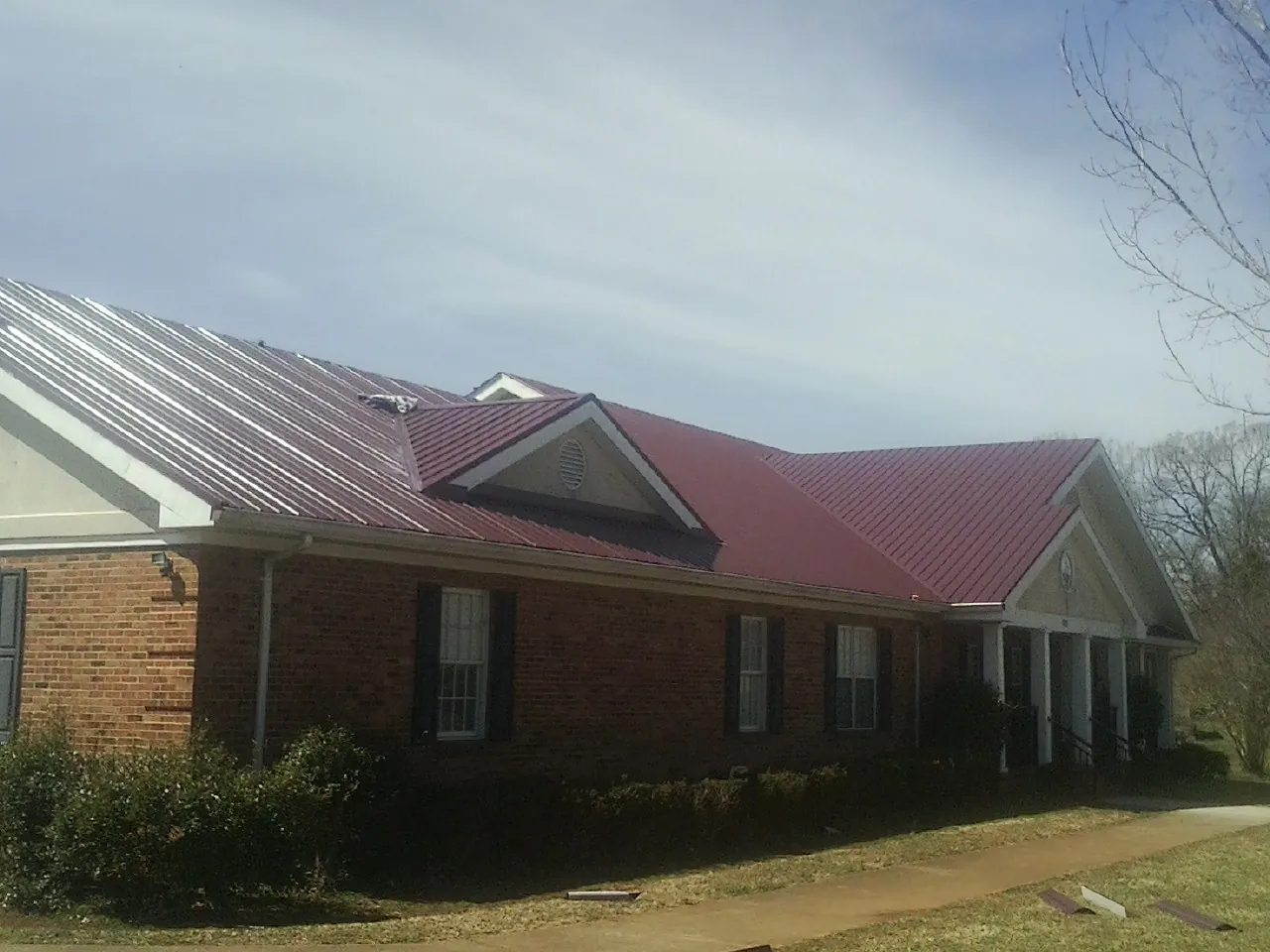 Red metal roof with gabled entries on a long brick building, from a Hail Damage Roof Repair job in Mc Coy