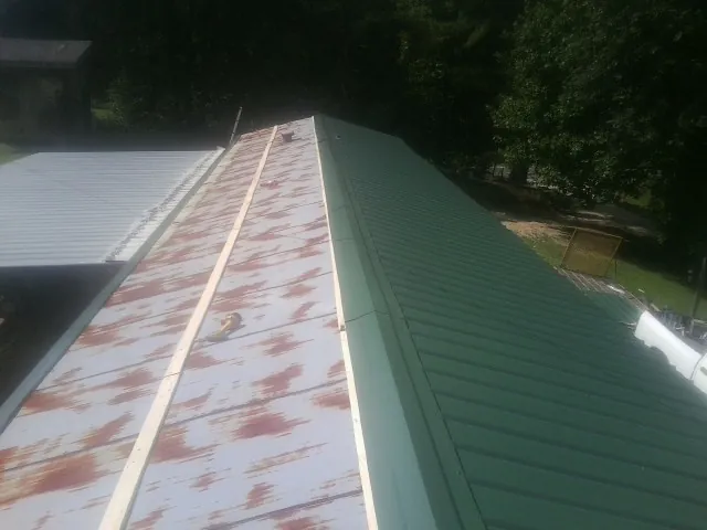 Old rusted panels beside newly installed green metal roofing — Wind Damage Roof Repair by Roofing Brothers in Mc Coy