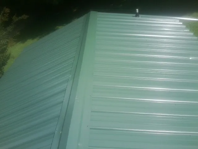 New green metal panels meeting at the ridge of a roof — Flat Roof Repair work by our crew in Mc Coy