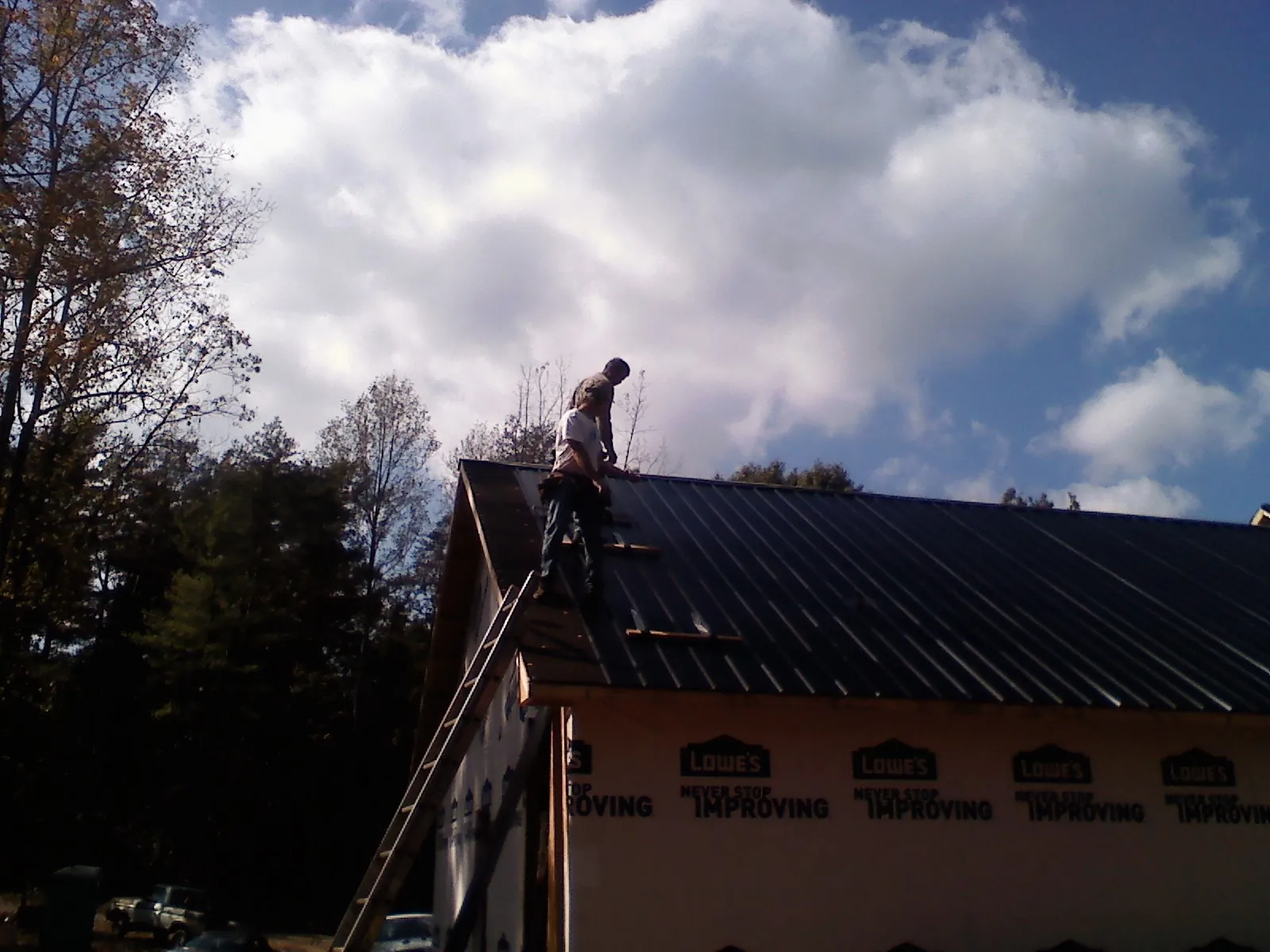 Roofer fastening dark metal panels high against a cloudy sky, from a Roof Inspection job in Mc Coy