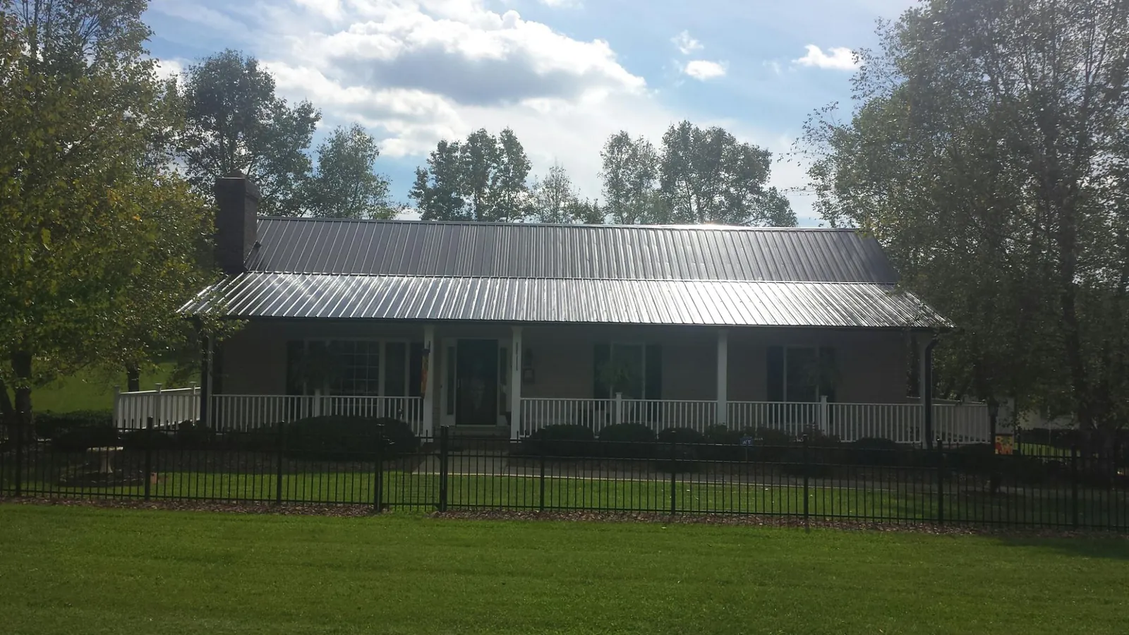 Gray metal roof on a brick ranch with a full width front porch — Gutter Guard Installation work by our crew in Mc Coy