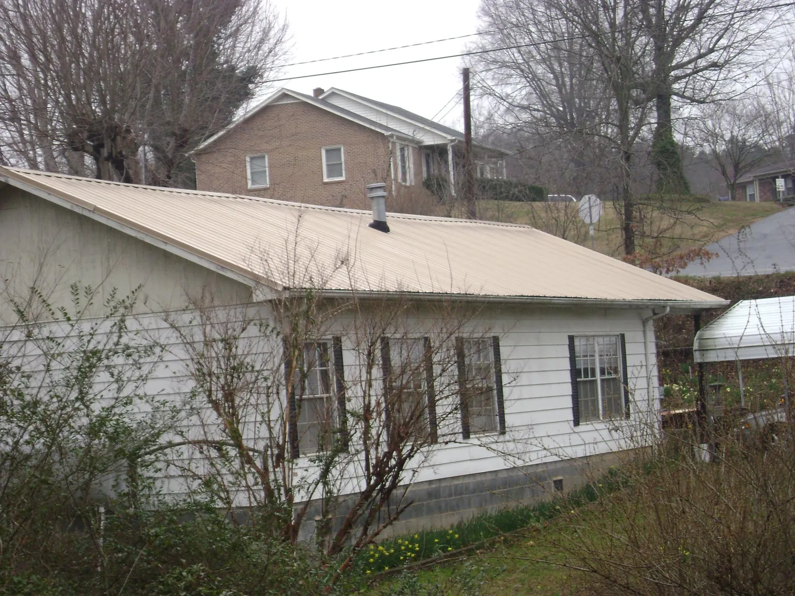 Tan metal roof on a white sided house set into a hillside — Commercial Roofing by Roofing Brothers in Mc Coy